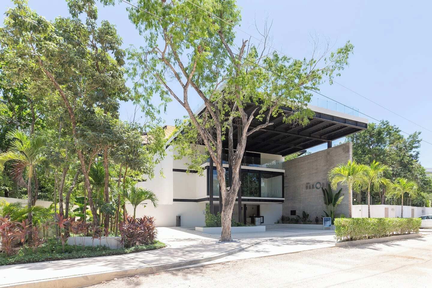 Un bâtiment moderne doté d’une entrée abritée, entouré d’arbres et de verdure.
