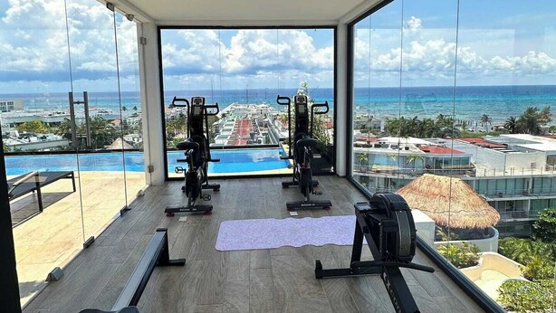 Ein Fitnessraum mit Trainingsgeräten und Blick auf einen Pool sowie Gebäude.