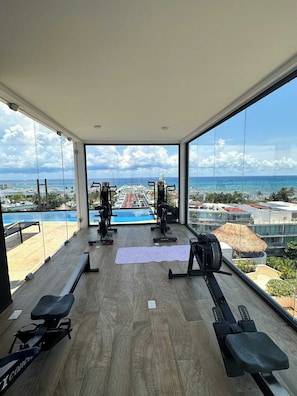 A gym with exercise equipment and a view of a swimming pool and buildings. - Best Location studio steps to the beach (Playa del Carmen)