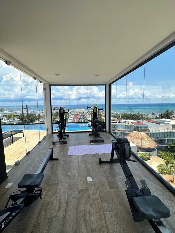 Ein Fitnessraum mit Trainingsgeräten und Blick auf einen Pool sowie Gebäude.