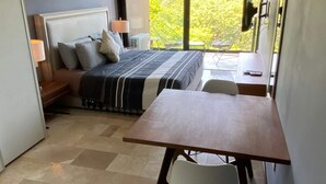 Ein Schlafzimmer mit Bett, Nachttisch, Lampe und Blick auf Grün.