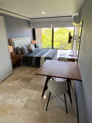 Ein Schlafzimmer mit Bett, Nachttisch, Lampe und Blick auf Grün.