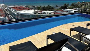Ein Pool mit Liegestühlen, Blick auf das Meer und Gebäude im Hintergrund.