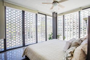 A bedroom with a bed, a ceiling fan, and large windows with a view of high-rise buildings. - Romantic Zone studio with Panoramic Pool (Puerto Vallarta)
