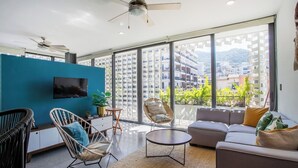Una sala de estar moderna con televisor, sofás, sillones y un balcón con vistas a la ciudad.