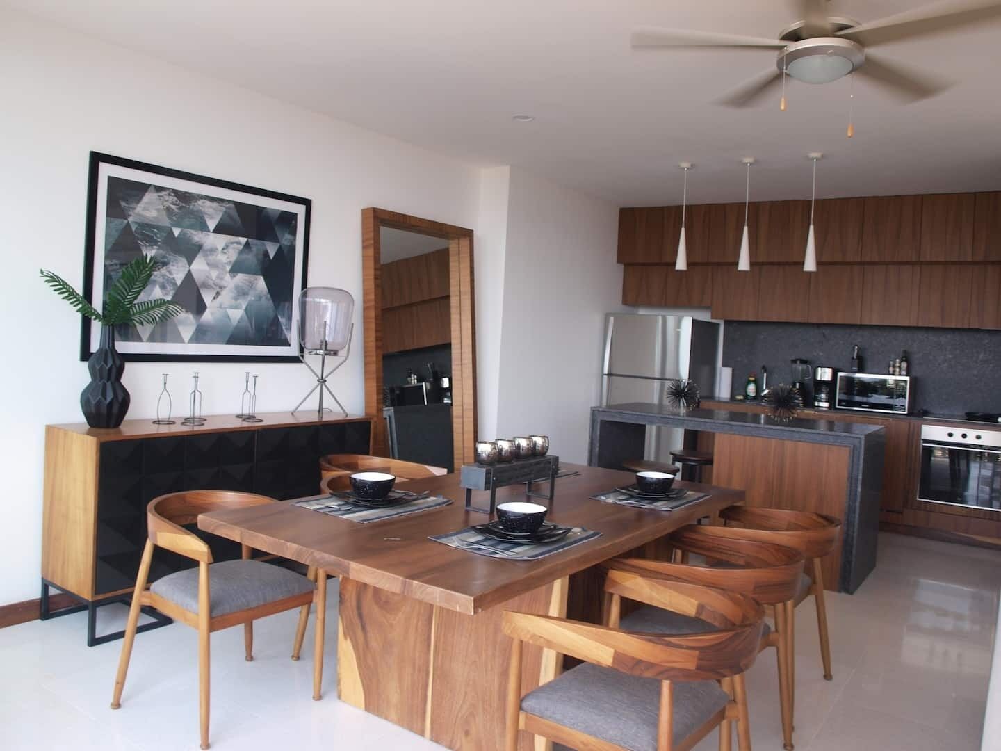 Une cuisine moderne avec des meubles en bois, un îlot central, des appareils en acier inoxydable et des luminaires suspendus.