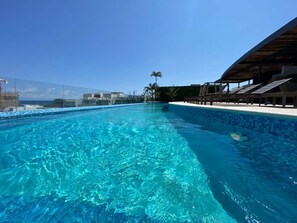 Ein klares, blaues Schwimmbecken mit Blick auf den Ozean und Palmen im Hintergrund.