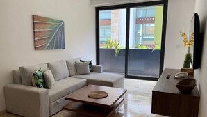 En moderne stue med en hjørnesofa, et sofabord, et fladskærms-tv og en skydedør, der fører ud til en balkon.