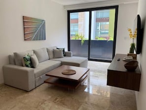 Ein modernes Wohnzimmer mit einer Eckcouch, einem Couchtisch, einem Flachbildfernseher und einer Glastür zum Balkon.