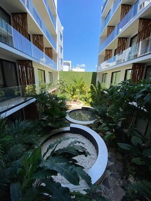 Ein moderner Hotelinnenhof mit einem zentralen, runden Wasserspiel, umgeben von üppiger Bepflanzung und einem Glasgeländer.