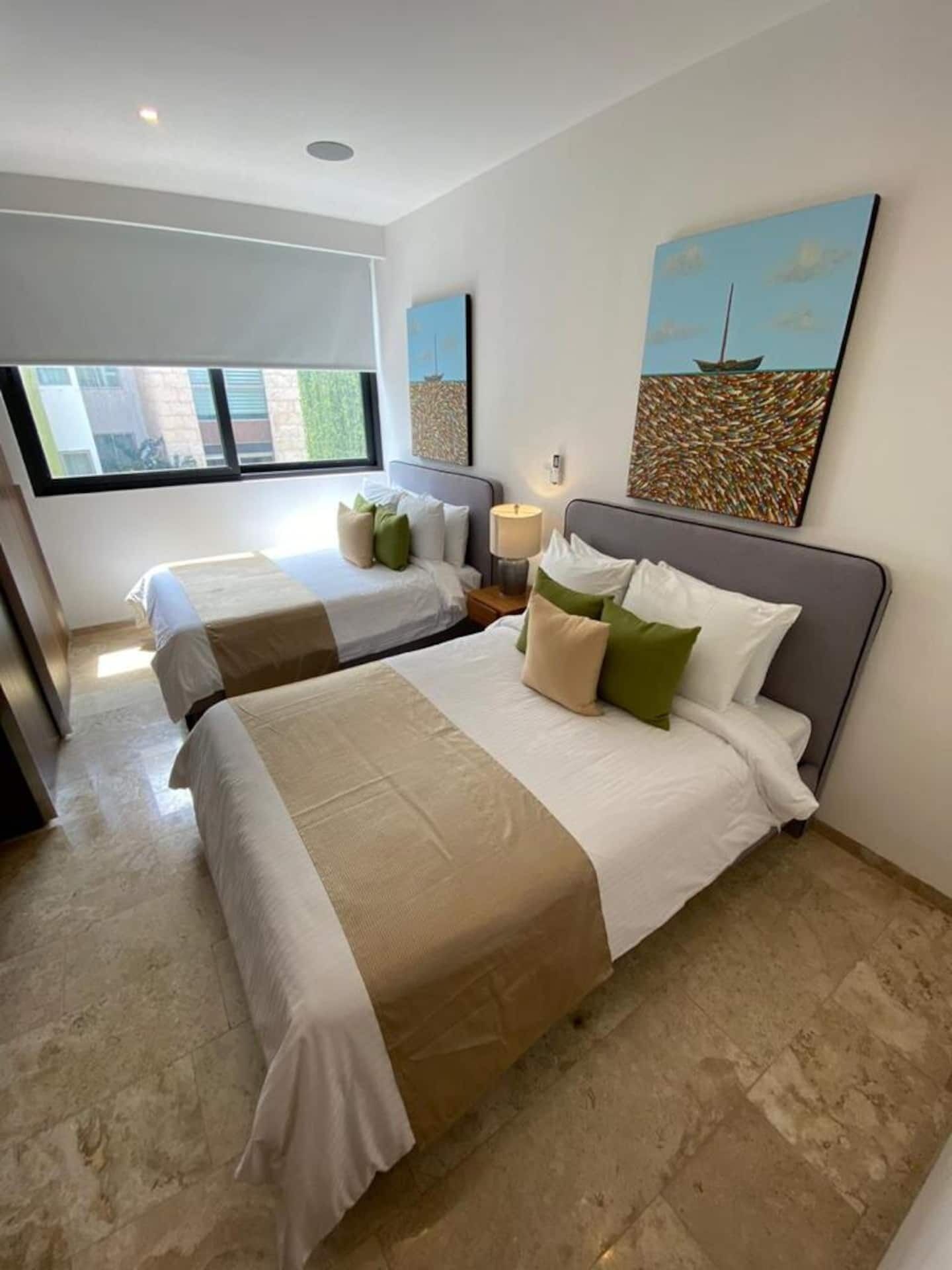Habitación de hotel con dos camas, un ventanal grande y obras de arte en las paredes.