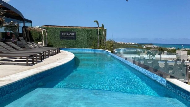 En pool med klart, blåt vand, liggestole og et skilt med teksten 'THE SHORE'.