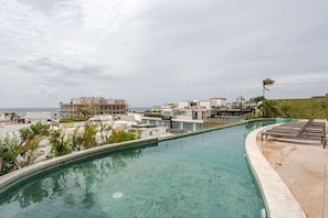A swimming pool with a curved edge, surrounded by a tiled deck and lounge chairs. - 3 Bdrm, Urban Luxury Suites with Infinity Pool (Playa del Carmen)