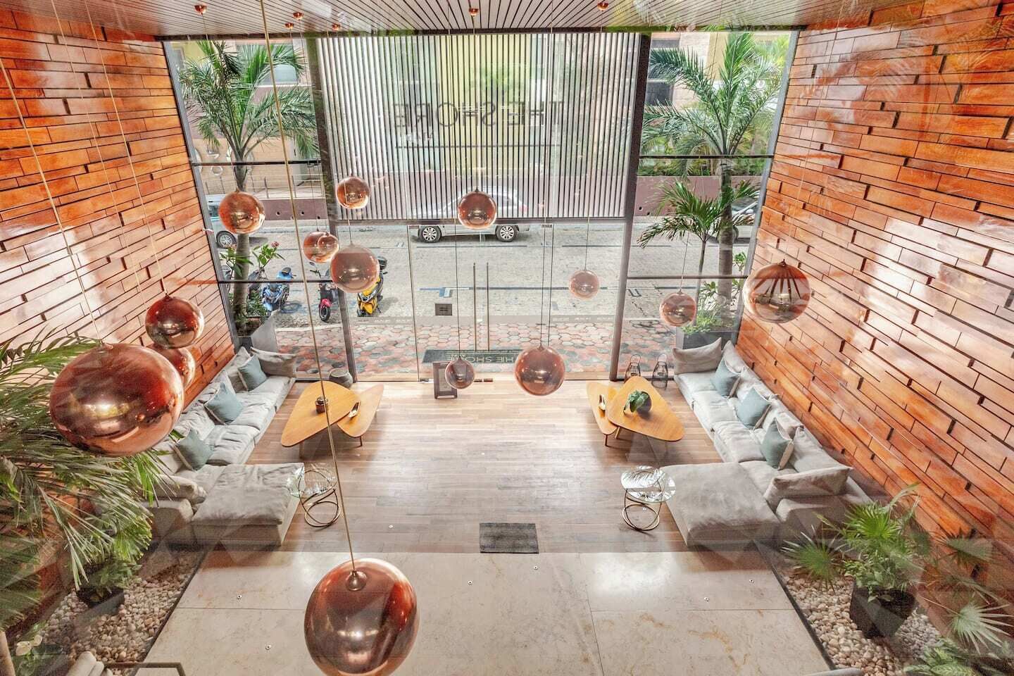 A modern interior with a central seating area, hanging spherical lights, and a view through a large window.