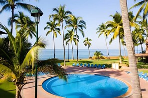 Una piscina con lettini, palme e vista sull'oceano.