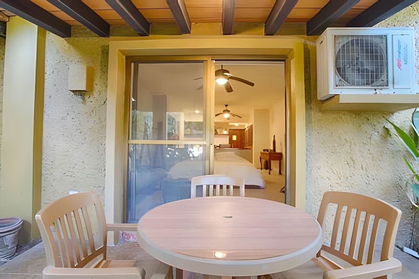 Une terrasse avec une table ronde et deux chaises, un climatiseur et un ventilateur de plafond.