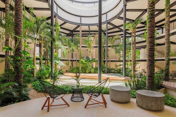 A spacious indoor garden with a central seating area, surrounded by lush greenery and a circular ceiling structure. - Boho Style Penthouse with Private Pool 150 Wifi (La Veleta)