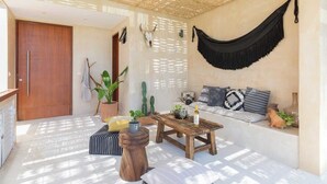 Una habitació il·luminada pel sol amb una hamaca, una taula de fusta, un sofà i plantes en testos.