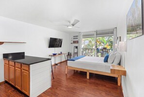 Ein Schlafzimmer mit Bett, Schreibtisch, Fernseher und einem Balkon mit Blick auf Grünflächen.