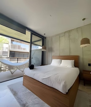 Ein modernes Schlafzimmer mit einem großen Bett, einer Hängematte und Blick auf Gebäude.
