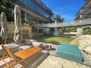 Ein Poolbereich mit Liegestühlen, Sonnenschirmen und einer Brücke.