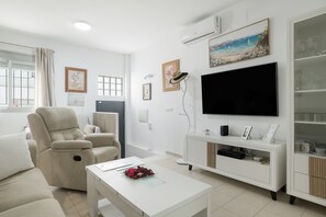 Una sala de estar moderna con un sofá beige, una mesa de centro blanca, un televisor de pantalla plana y un mueble de entretenimiento blanco.