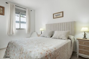 Un dormitori amb llit, làmpades de nit, una taula de nit, una cadira i una finestra amb cortines.