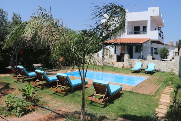 A pool area with lounge chairs, a swimming pool, and a modern two-story building.