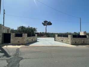 Ein gepflasterter Weg führt zu einem verschlossenen Eingang mit Steinmauern und einem Baum im Hintergrund.
