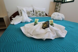 Ein Bett mit einer petrolfarbenen Steppdecke, weißen Handtüchern und zwei Flaschen Olivenöl.
