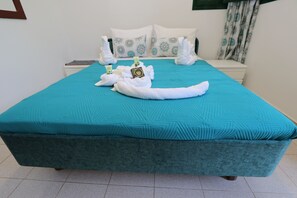 A bed with a teal bedspread, white pillows with blue patterns, and a white towel with a bottle of olive oil. - One beautiful accommodation with good atmosphere & comforts!!! (Greece City)