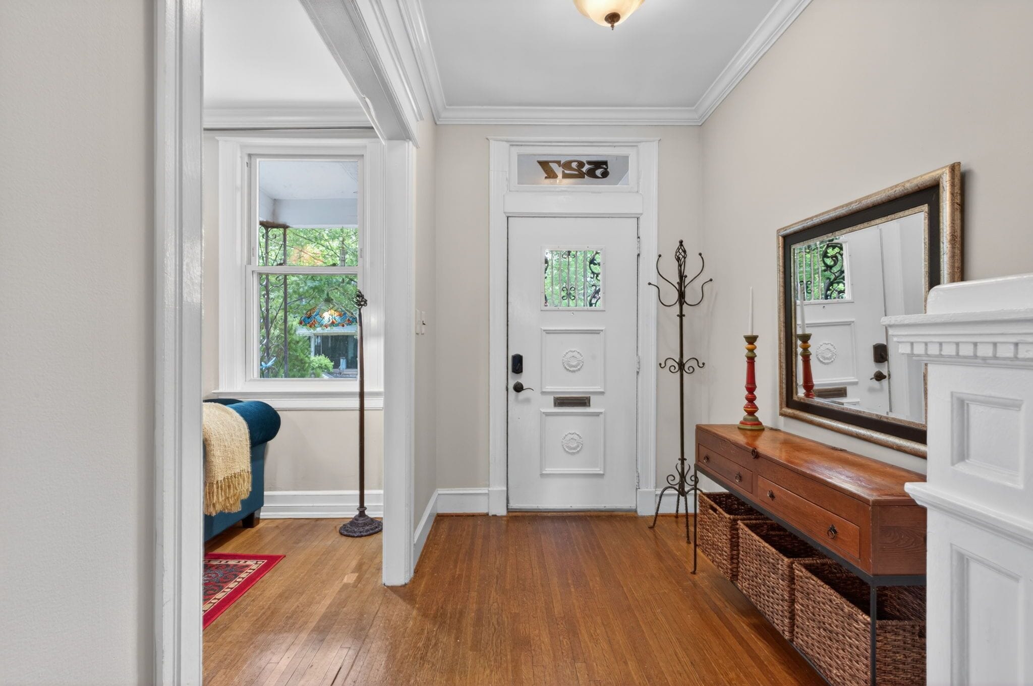A hallway with a white door, a blue sofa, a floor lamp, a mirror, and wicker baskets.