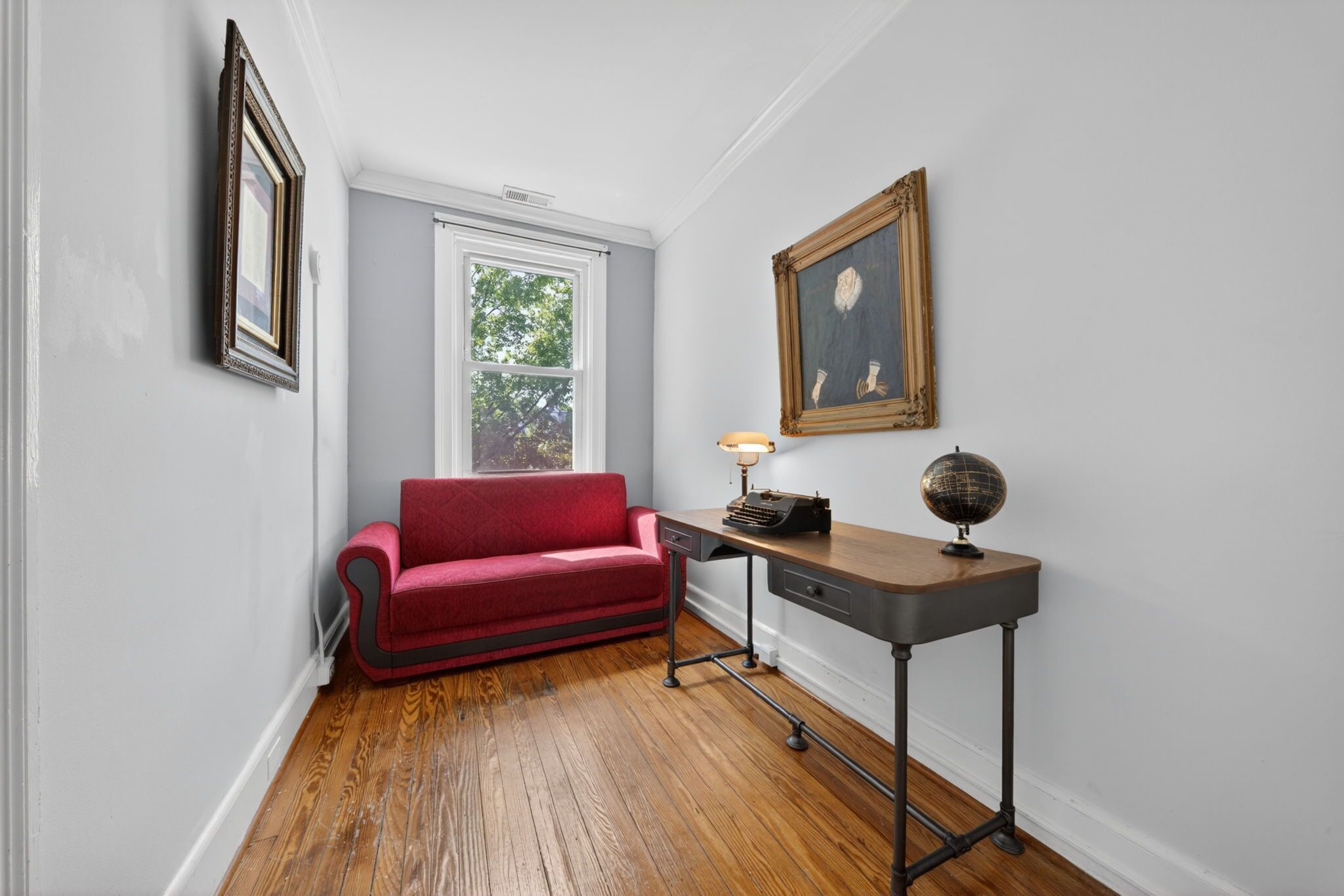 Ein Zimmer mit einem roten Sofa, einem Schreibtisch mit Globus und einem gerahmten Bild an der Wand.