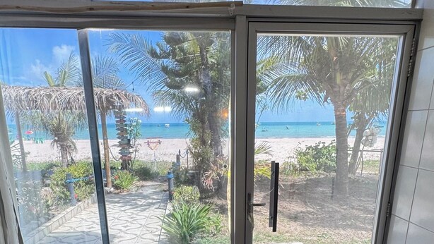 Ein Zimmer mit einem großen Glasfenster, das Blick auf einen Strand bietet, mit Fliesenboden und einer Bank.