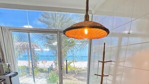 Ein Essbereich mit einem runden Holztisch, zwei Stühlen, einer Hängeleuchte und Blick auf den Strand durch große Fenster.