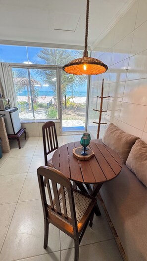 Ein Essbereich mit einem runden Holztisch, zwei Stühlen, einer Hängeleuchte und Blick auf den Strand durch große Fenster.