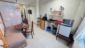 Eine kompakte Küche mit Essbereich, inklusive Tisch und Stühlen, einer Pendelleuchte, einer Mikrowelle und einer Kaffeemaschine.