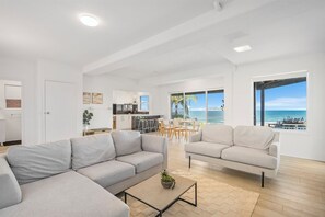 A modern living room with a sofa, coffee table, and a view of the ocean. - 22 Dent Crescent - Spacious Coastal Retreat with Stunning Ocean Views (Port Macquarie)