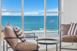 A room with a large window overlooking the ocean, two chairs with cushions, and a small round table. - 22 Dent Crescent - Spacious Coastal Retreat with Stunning Ocean Views (Port Macquarie)