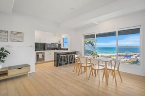 A modern kitchen with a view of the ocean, a dining area with chairs, and a large window. - 22 Dent Crescent - Spacious Coastal Retreat with Stunning Ocean Views (Port Macquarie)