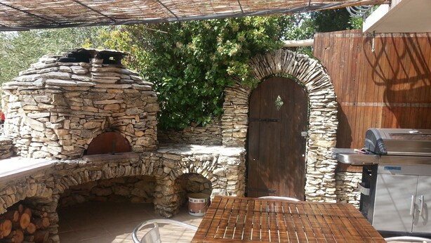Une terrasse extérieure avec un four en pierre, une porte en bois et un barbecue.