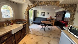 Une cuisine avec une arche en pierre donnant sur un espace de vie comprenant un coin repas et un téléviseur.