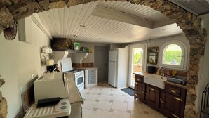 Une cuisine avec des murs en pierre, un poêle, un réfrigérateur et une fenêtre donnant sur un paysage agréable.