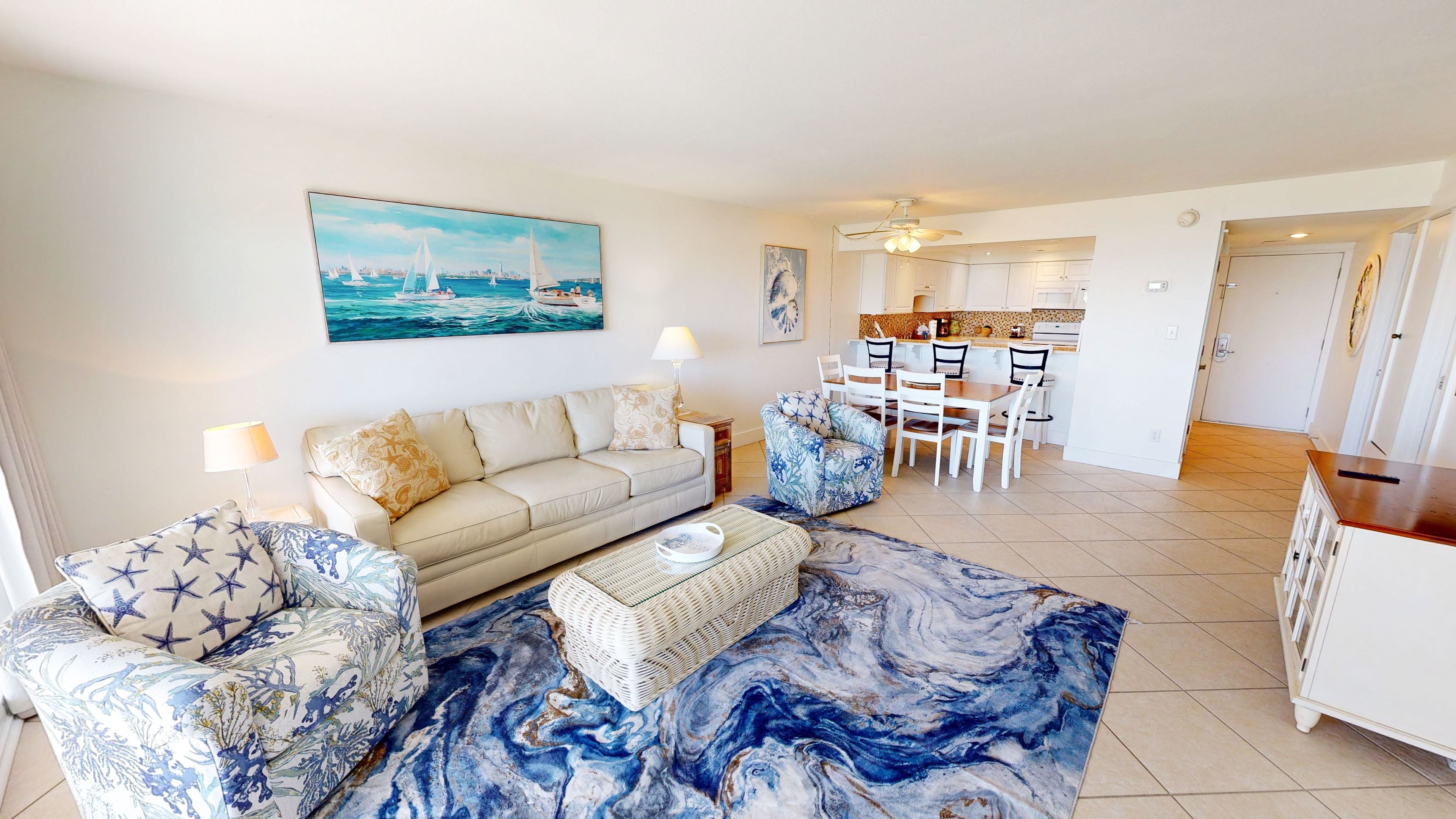 A living room with a sofa, chairs, a dining table, and a kitchen in the background.