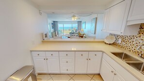 A kitchen with white cabinets, a stainless steel sink, and a tiled backsplash. - Beach House 101c 2 Bedroom Condo (Miramar Beach)