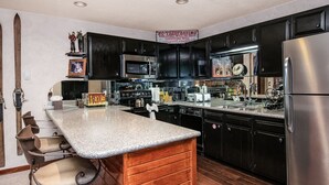 A kitchen with dark cabinets, a stainless steel refrigerator, a wooden island, and a bar stool. - Scorpio #101 2 Bedroom Condo (Vail)