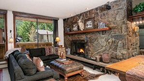 A cozy living room with a stone fireplace, a sofa, a coffee table, and a rug. - Scorpio #101 2 Bedroom Condo (Vail)