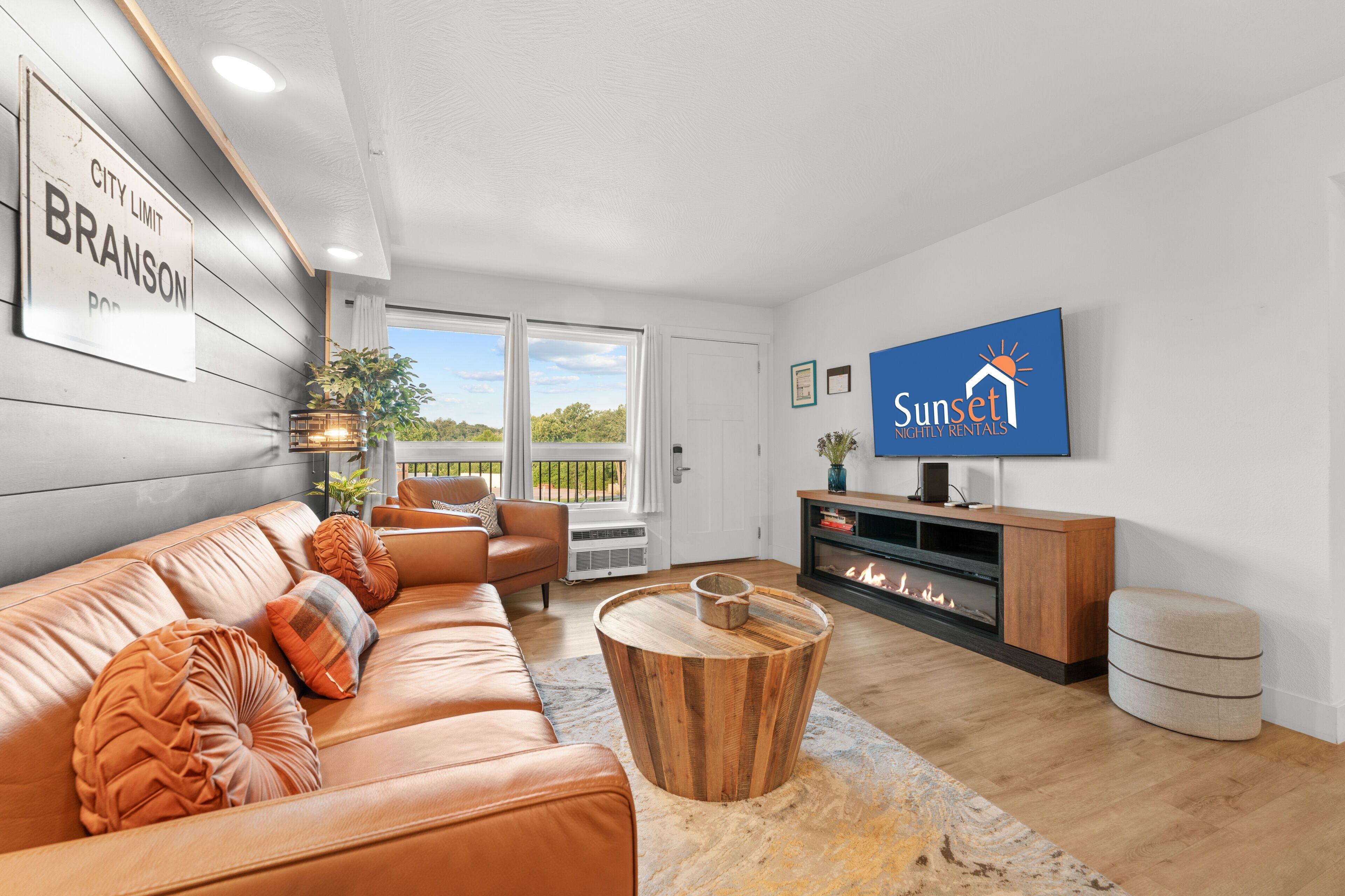 A modern living room with a leather sofa, a wooden coffee table, a fireplace, and a television.