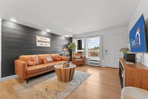 A modern living room with a leather sofa, a wooden coffee table, and a view of the city. - Rc305a- The Landing Pad 2 Bedroom Condo (Branson)