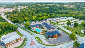 An aerial view of a town with a prominent building with a blue roof, a swimming pool, and a large parking lot. - Rc305a- The Landing Pad 2 Bedroom Condo (Branson)